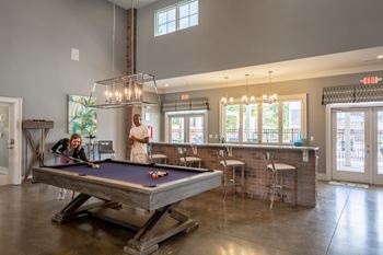 a man and woman playing pool in a clubhouse with a bar and a pool table